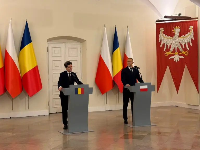Nicușor Dan stând la un pupitru cu steagul României în timpul unei conferințe oficiale, alături de un alt oficial la un pupitru cu steagul Poloniei