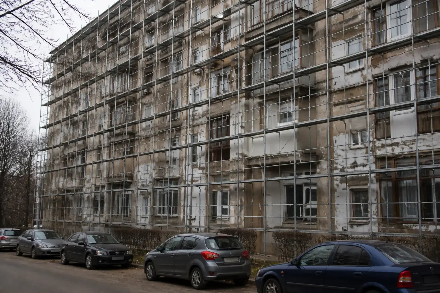 O fațadă a unui bloc vechi de locuințe, aflat în curs de renovare sau consolidare, acoperită integral de schele metalice