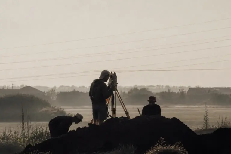 Surveyors using a total station on a tripod in a misty field for land measurement